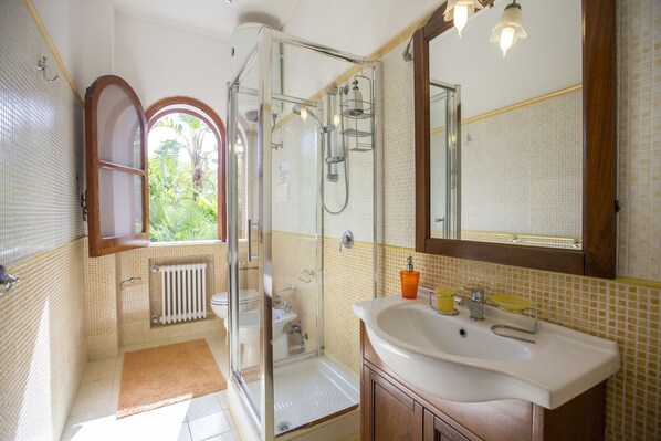 Un baño con ducha de vidrio, un lavamanos blanco y un espejo sobre él.