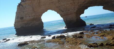 Formación rocosa natural con un arco parecido a una cueva sobre una playa.