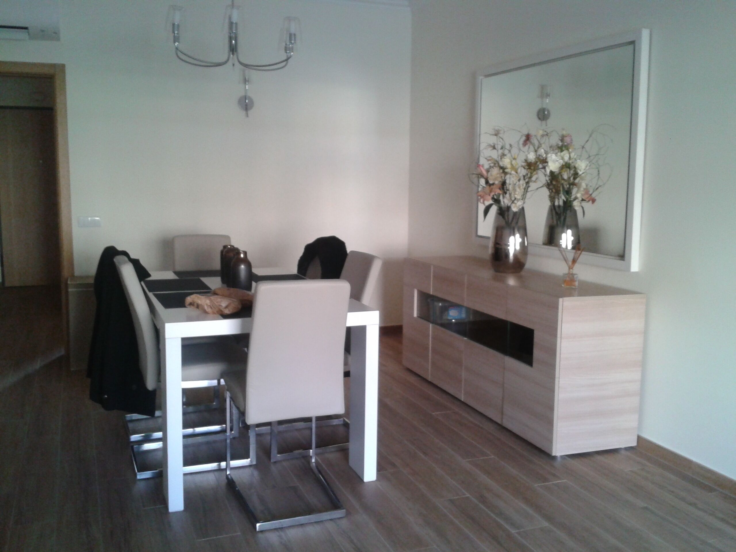 A modern dining area with a white table, chairs, and a wooden cabinet with a mirror above it.