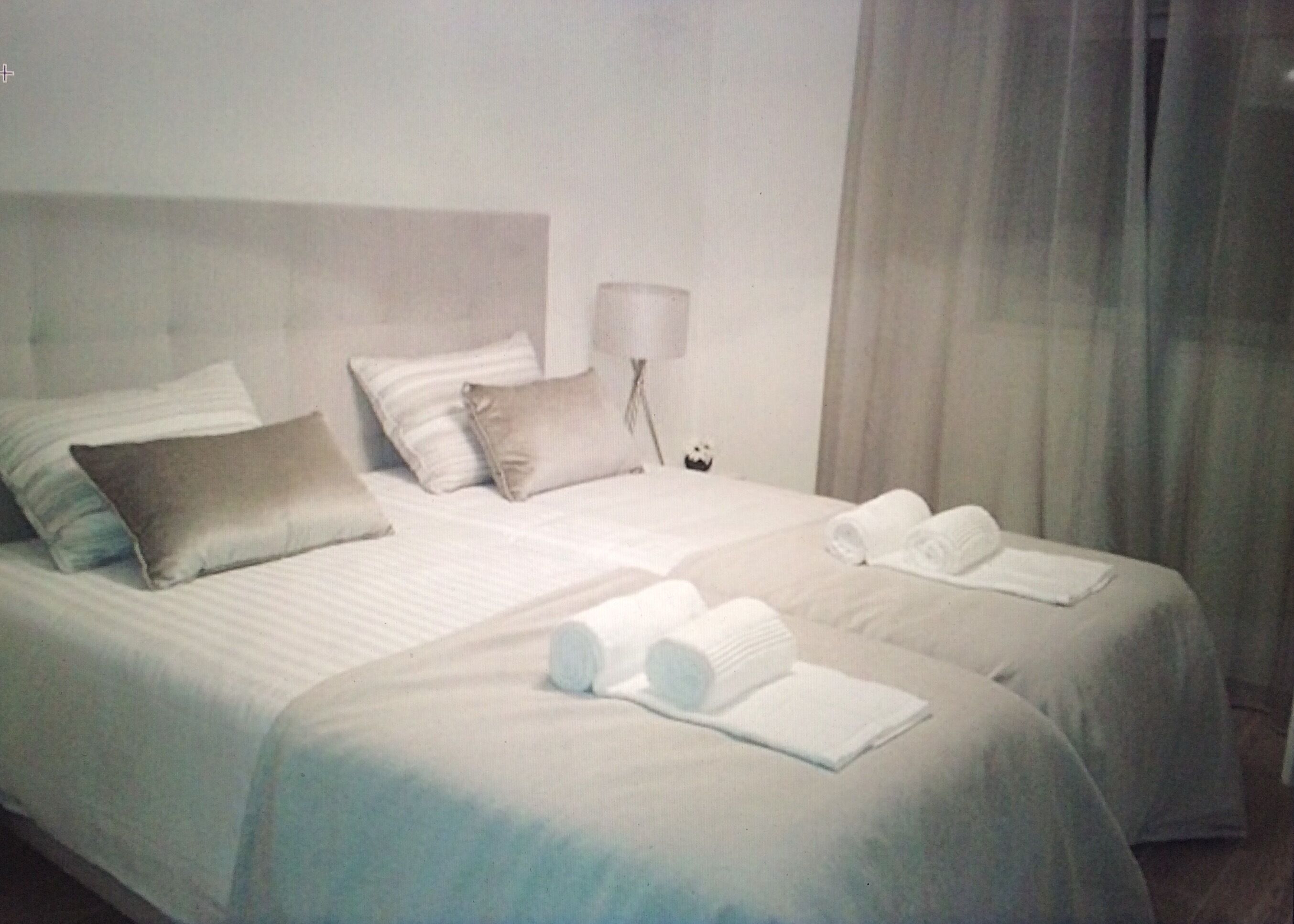 A hotel room with two beds, a nightstand with a lamp, and towels on the beds.