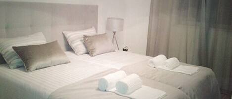 A hotel room with two beds, a nightstand with a lamp, and towels on the beds.