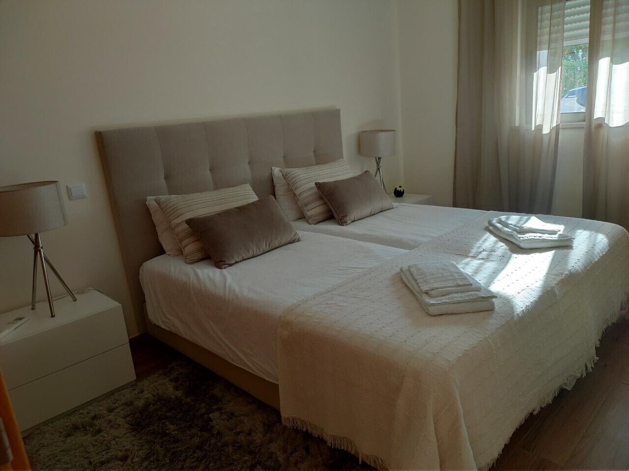 A double bed with a headboard, two bedside tables with lamps, and a window with curtains.