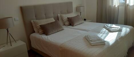 A double bed with a headboard, two bedside tables with lamps, and a window with curtains.