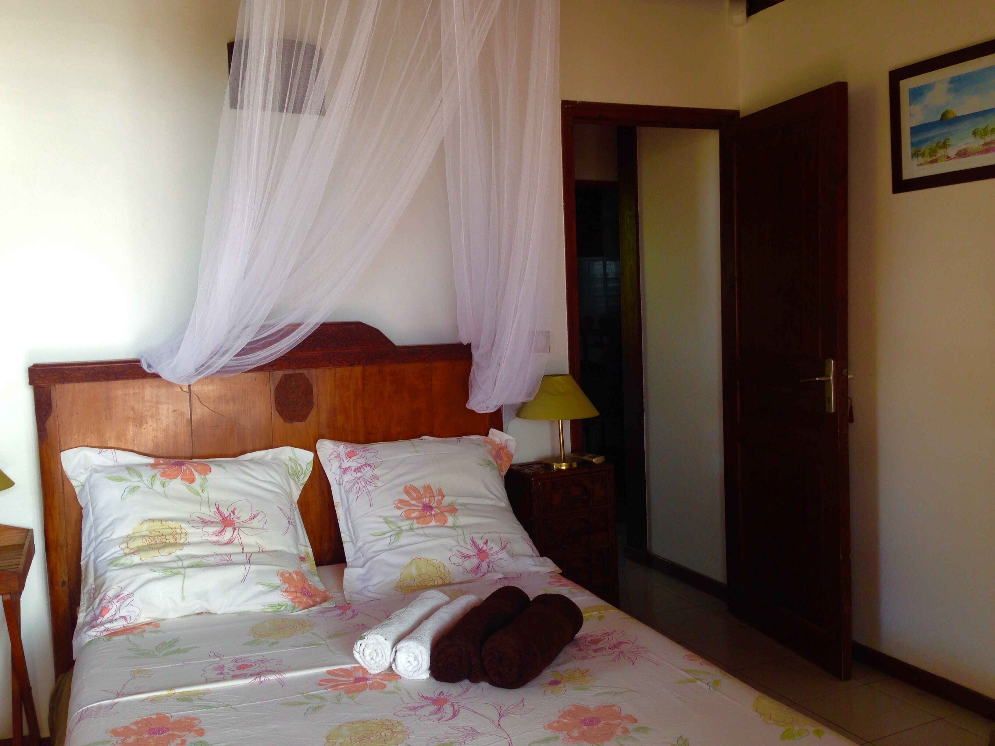 Uma cama com roupa de cama floral, uma cabeceira de madeira e uma mesinha de cabeceira com abajur.