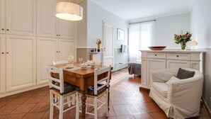 A dining area with a wooden table and chairs, a white sofa, and a cabinet with a bowl and flowers on top. - Paradiso | Romantic open space in the heart of Rome (Roma)