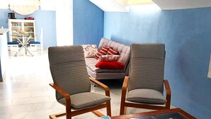 A modern living room with a glass coffee table, two armchairs, a sofa, and a dining area in the background.
