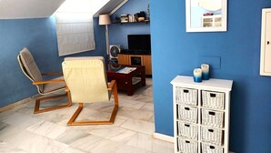 A room with a blue wall, a ceiling fan, a TV, a bookshelf, and a chair.