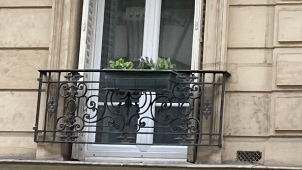 A building facade with a balcony featuring ornate metal railings and a window with a white frame.