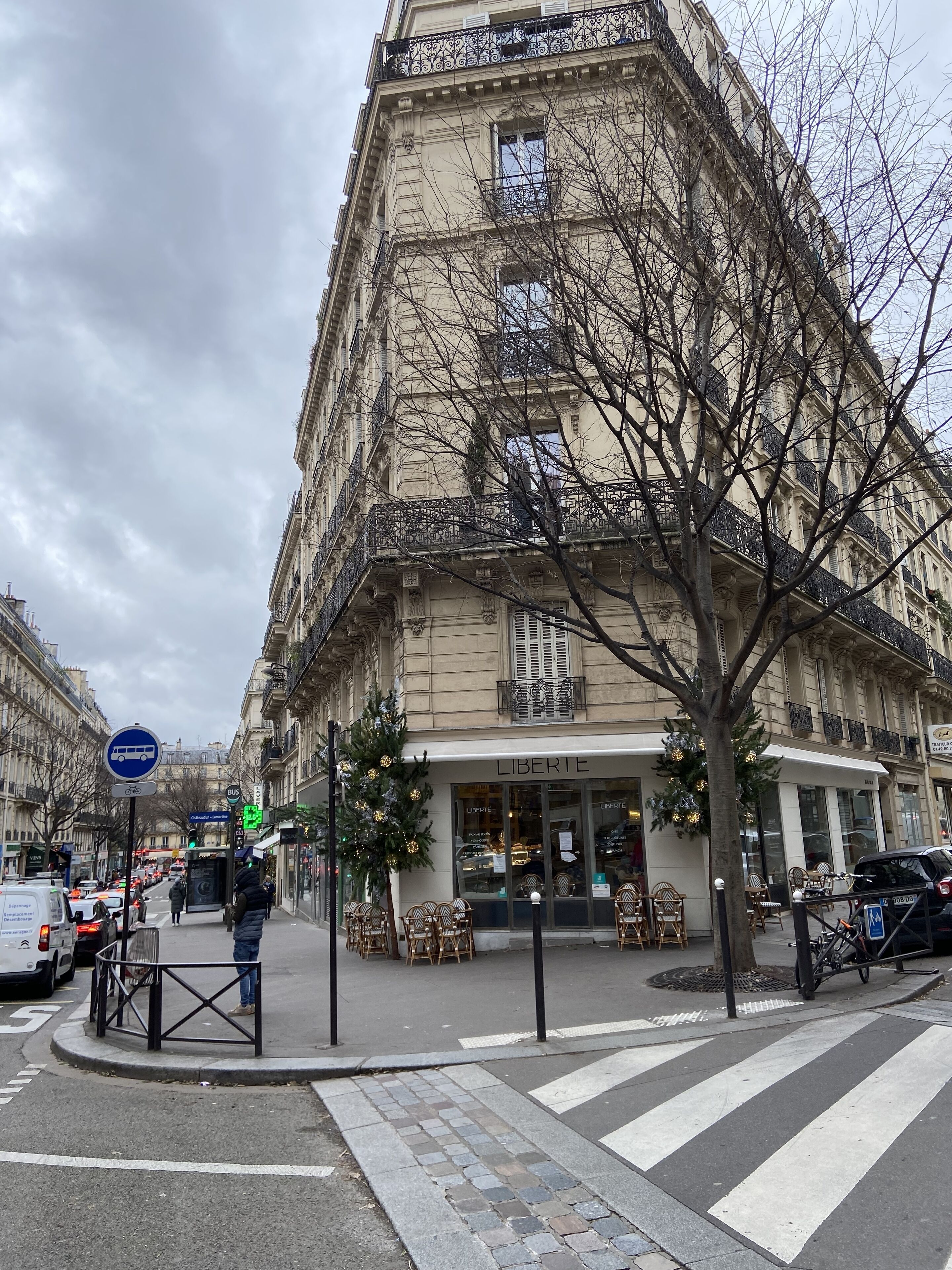 A street view with a building labeled "LIBERTE" featuring a ground-floor café with outdoor seating.