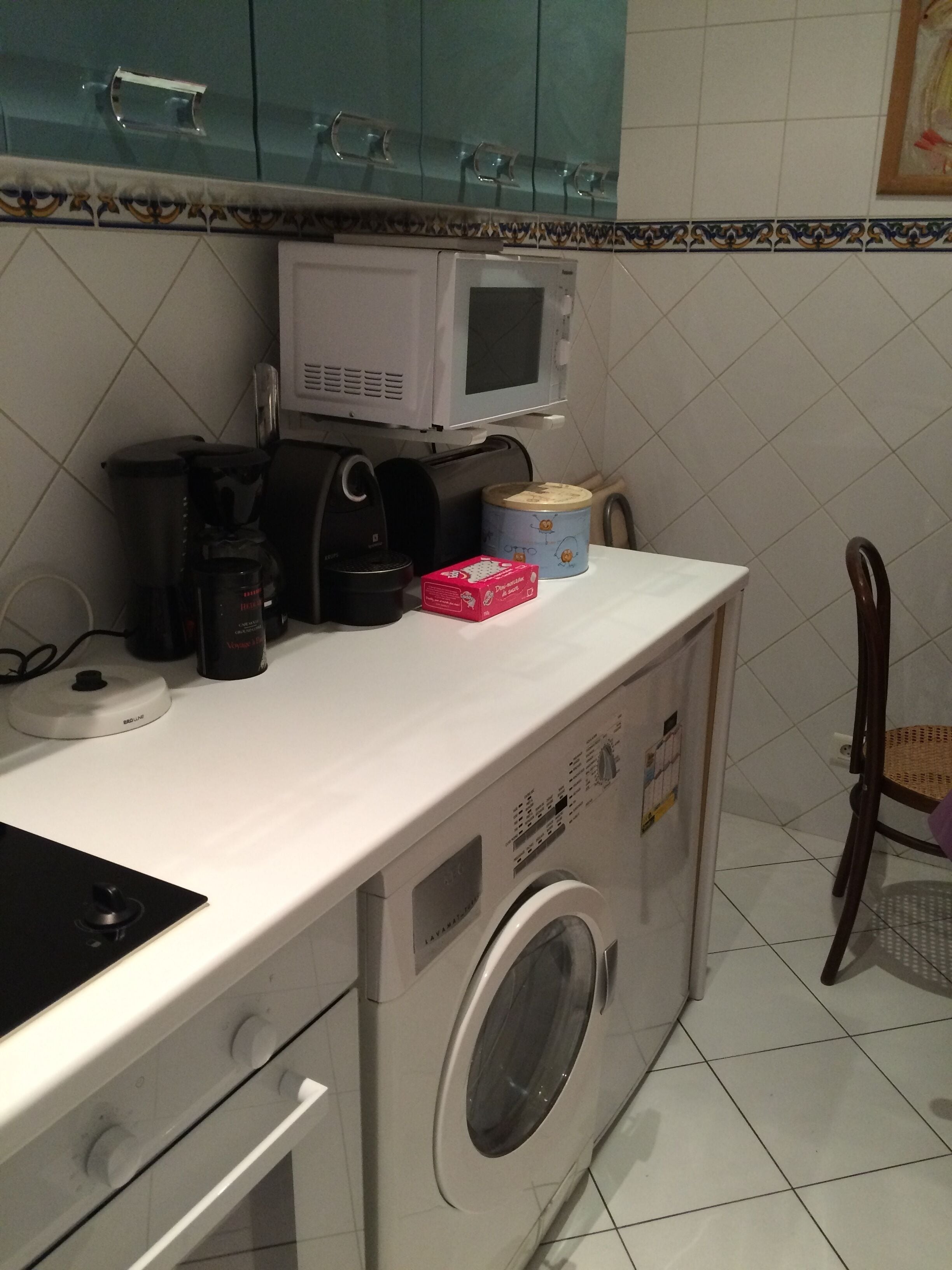 A compact kitchen with a microwave, coffee maker, and a washing machine.