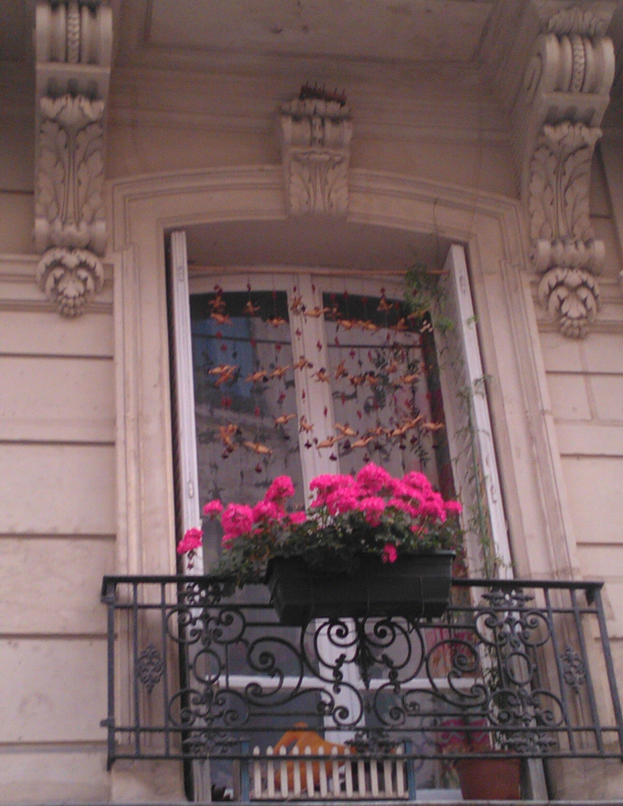 A balcony with wrought iron railings and a flower box with pink flowers.