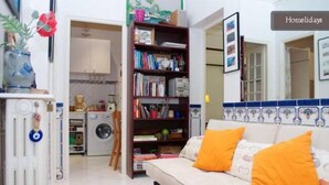 A living room with a sofa, a bookshelf, and a kitchen area in the background.