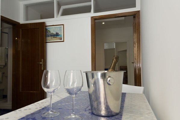 A room with a wooden door, a painting of a beach scene, and a table with two wine glasses and a champagne bucket.