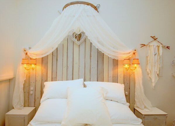 A bed with a canopy, two bedside lamps, a decorative wall hanging, and a small bedside table. - PATIO HOUSE balcony shabby chic home in Spello (Spello)