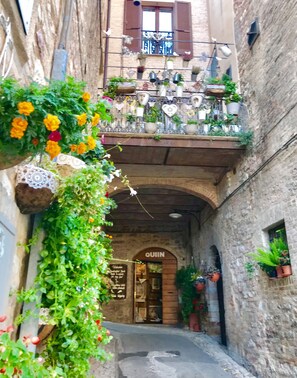A narrow alleyway with a building on the right featuring a balcony with potted plants and a sign reading "QUIN". - PATIO HOUSE balcony shabby chic home in Spello (Spello)