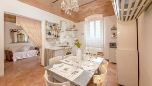 A dining area with a table set for four, a chandelier, and a kitchen in the background. - PATIO HOUSE balcony shabby chic home in Spello (Spello)