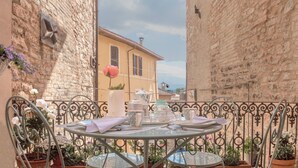 A round metal table set with white teapots, cups, and saucers, surrounded by metal chairs, with potted plants and a pink flower on the balcony railing. - PATIO HOUSE balcony shabby chic home in Spello (Spello)