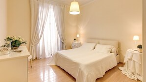 Un dormitorio con cama, mesita de noche, lámpara y ventana con cortinas.
