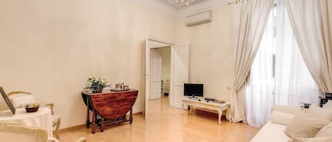 A spacious living room with a wooden floor, a white sofa, a wooden coffee table, a TV, and a chandelier.