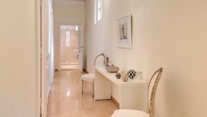 Un pasillo con una puerta blanca al final, un banco blanco y una mesita con adornos.
