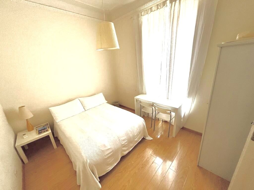 A bedroom with a bed, bedside table, lamp, and a window with curtains.