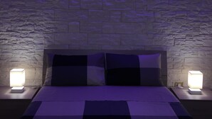 A bedroom with a stone wall, a bed with a checkered bedspread, and two bedside lamps. - Apartment in Ortigia furnished and equipped with all comforts (Siracusa)