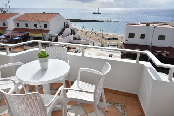 A balcony with white chairs and a table, overlooking a beach and a pier.