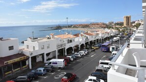A coastal street with parked cars, a bus, and a building with a sign advertising a wide range of draught beers. - The Outside Christians, Fantastic Views. (Arona)