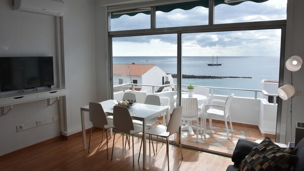 A modern living room with a large window overlooking the sea, a dining area with white furniture, and a flat-screen TV mounted on the wall. - The Outside Christians, Fantastic Views. (Arona)