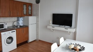 A compact kitchen with wooden cabinets, a washing machine, a microwave, a refrigerator, and a flat-screen TV mounted on the wall. - The Outside Christians, Fantastic Views. (Arona)