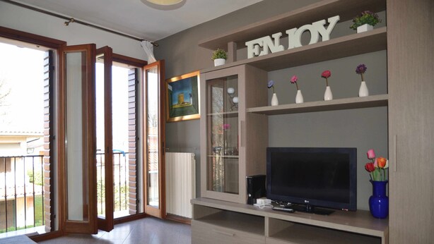 Ein Wohnzimmer mit Fernseher, einer Glasvitrine mit Blumen und einer Balkontür.