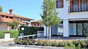 Ein modernes, zweistöckiges Haus mit einem Balkon, einem kleinen Baum im Vorgarten und blauem Himmel.