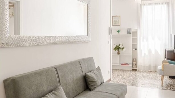 Ein modernes Wohnzimmer mit einem grauen Sofa, einem großen Spiegel und einer Chandelüster.