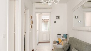 Ein Flur mit einem grauen Sofa, einer Chandelierleuchtre und einem Spiegel an der Wand.