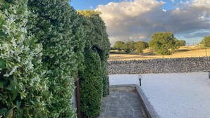 Un chemin de pierres menant à un mur blanc, entouré d’une végétation luxuriante et d’un autre mur en pierre.