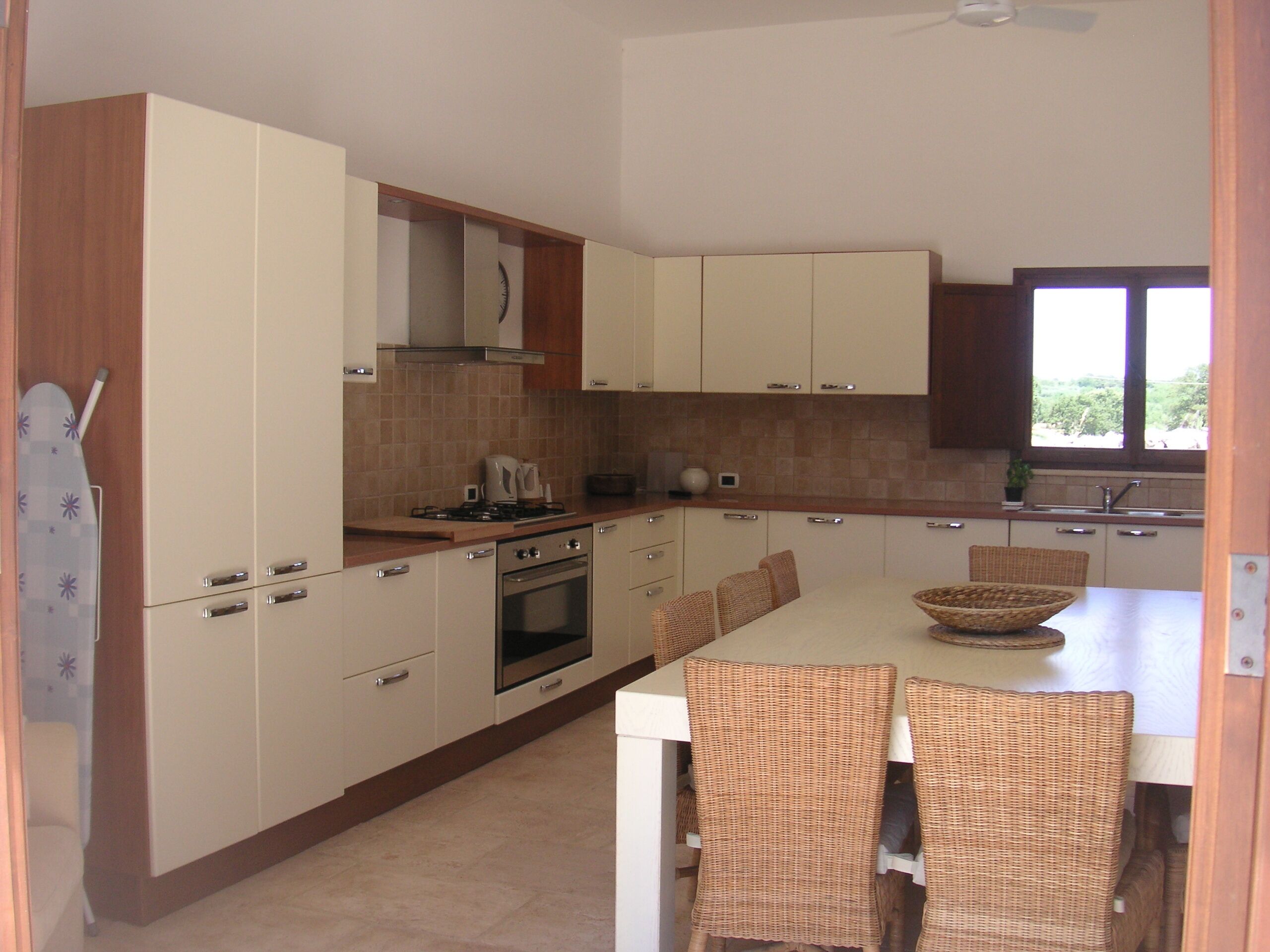 Una cocina moderna con armarios blancos, estufa a gas, horno y comedor con sillas de mimbre y una isla grande.