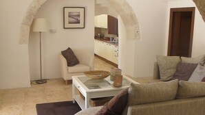 Un salon avec un canapé, une table basse et une lampe. On peut apercevoir une cuisine à travers une arche.
