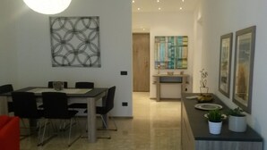 A dining area with a table and chairs, a hallway leading to a kitchen, and a living area with a sofa and a coffee table. - Exclusive apartment of 120 sqm, 4-6 sleeps, private parking (Milano)