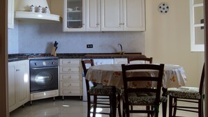 Een kleine keuken met witte kastjes, een fornuis en een eettafel met stoelen.