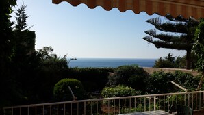Een balkon met uitzicht op zee, omringd door groen en een tafel met stoelen.