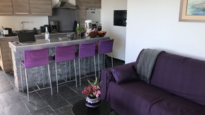 Una cocina moderna con una isla central, taburetes de bar morados y un sofá morado en la sala de estar.