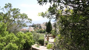 Vista de un pueblo costero con edificios de piedra, abundante vegetación y cielo despejado.
