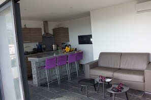 Una cocina moderna con una isla central, taburetes de bar, un sofá y una pequeña mesa con una vela.