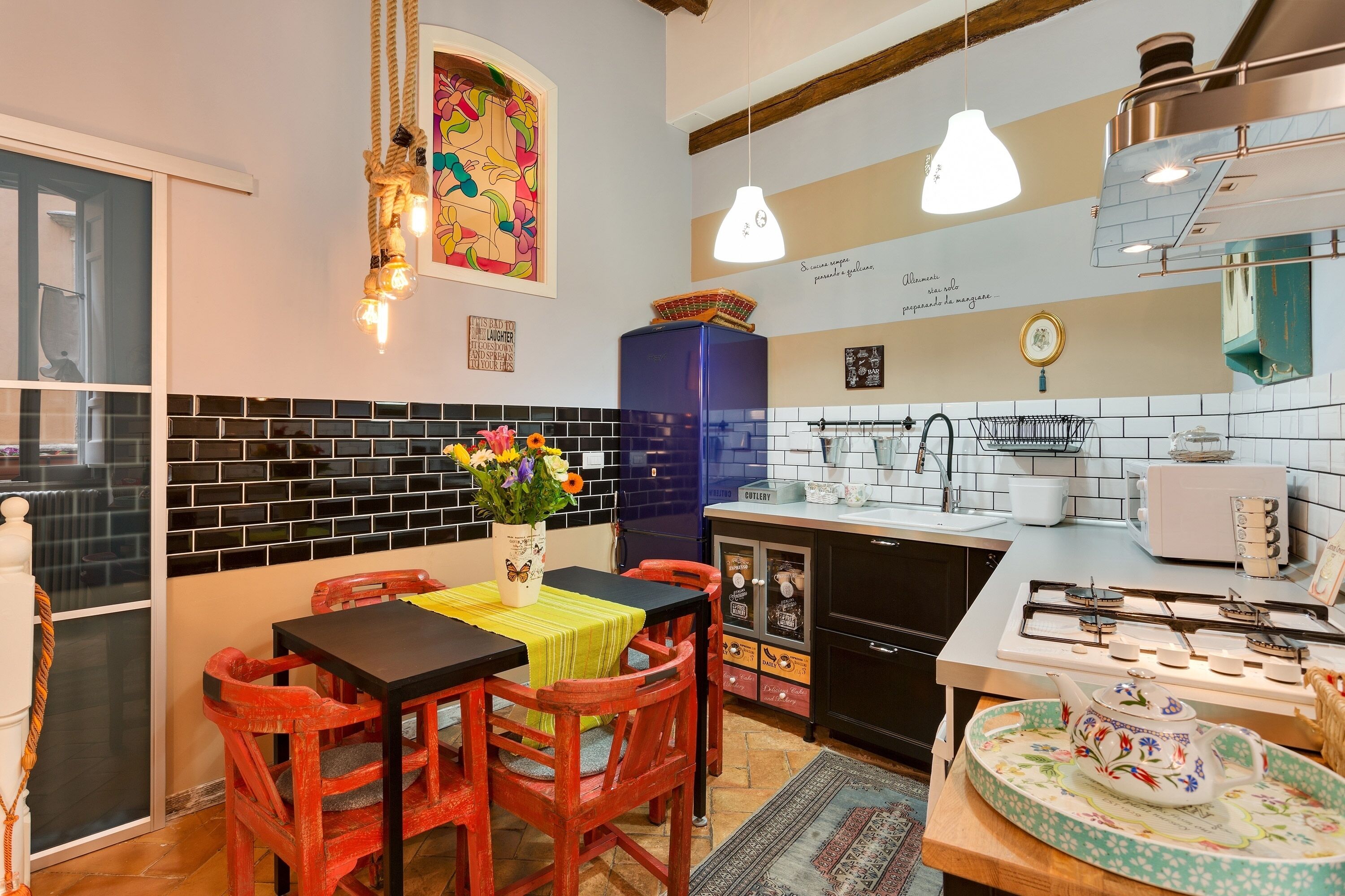 A compact kitchen with a dining area, featuring a black tiled backsplash, a blue cabinet, and a gas stove.