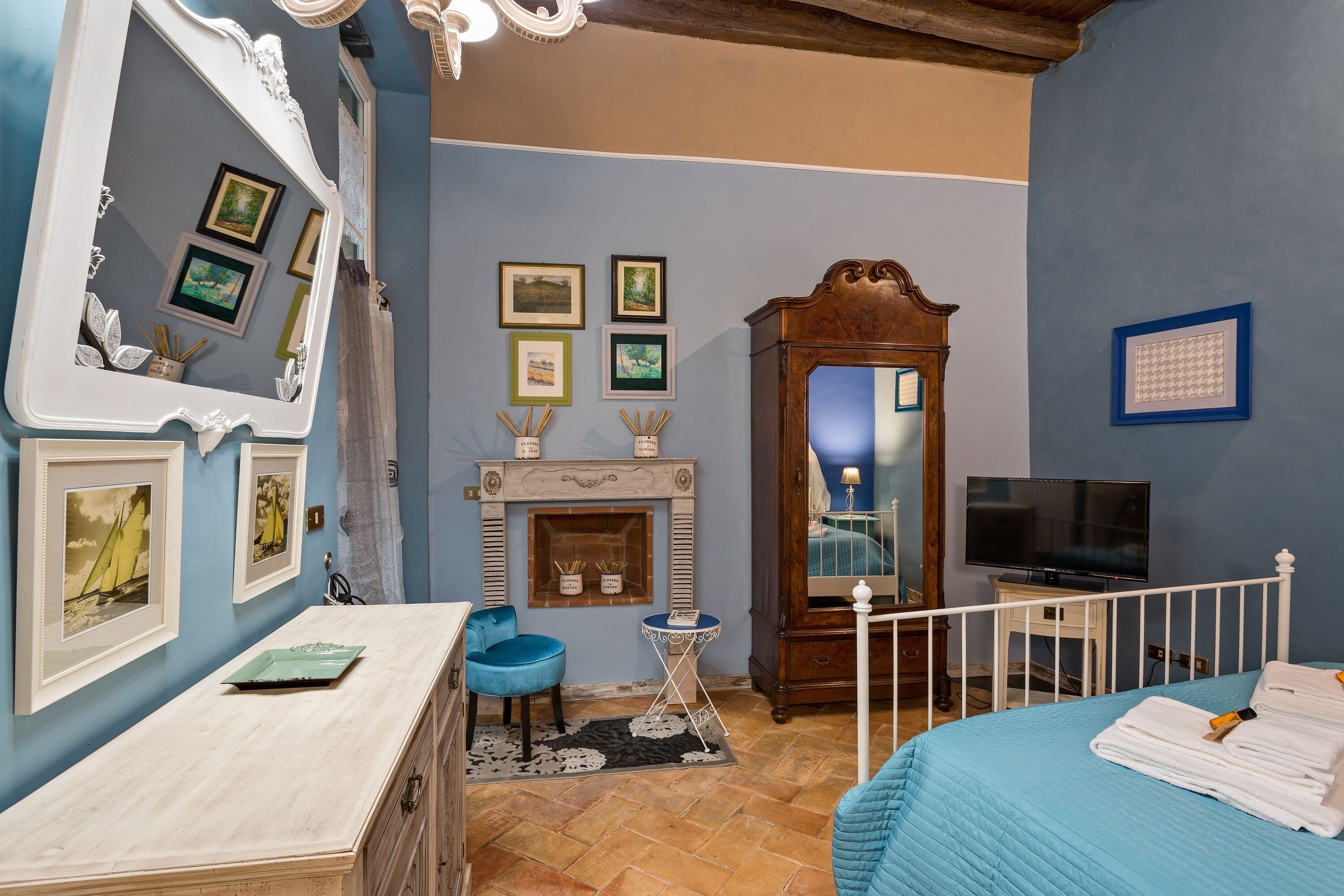 A room with a fireplace, a TV, a bed with towels, a blue chair, and a mirror with pictures on the wall.