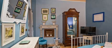 A room with a fireplace, a TV, a bed with towels, a blue chair, and a mirror with pictures on the wall.