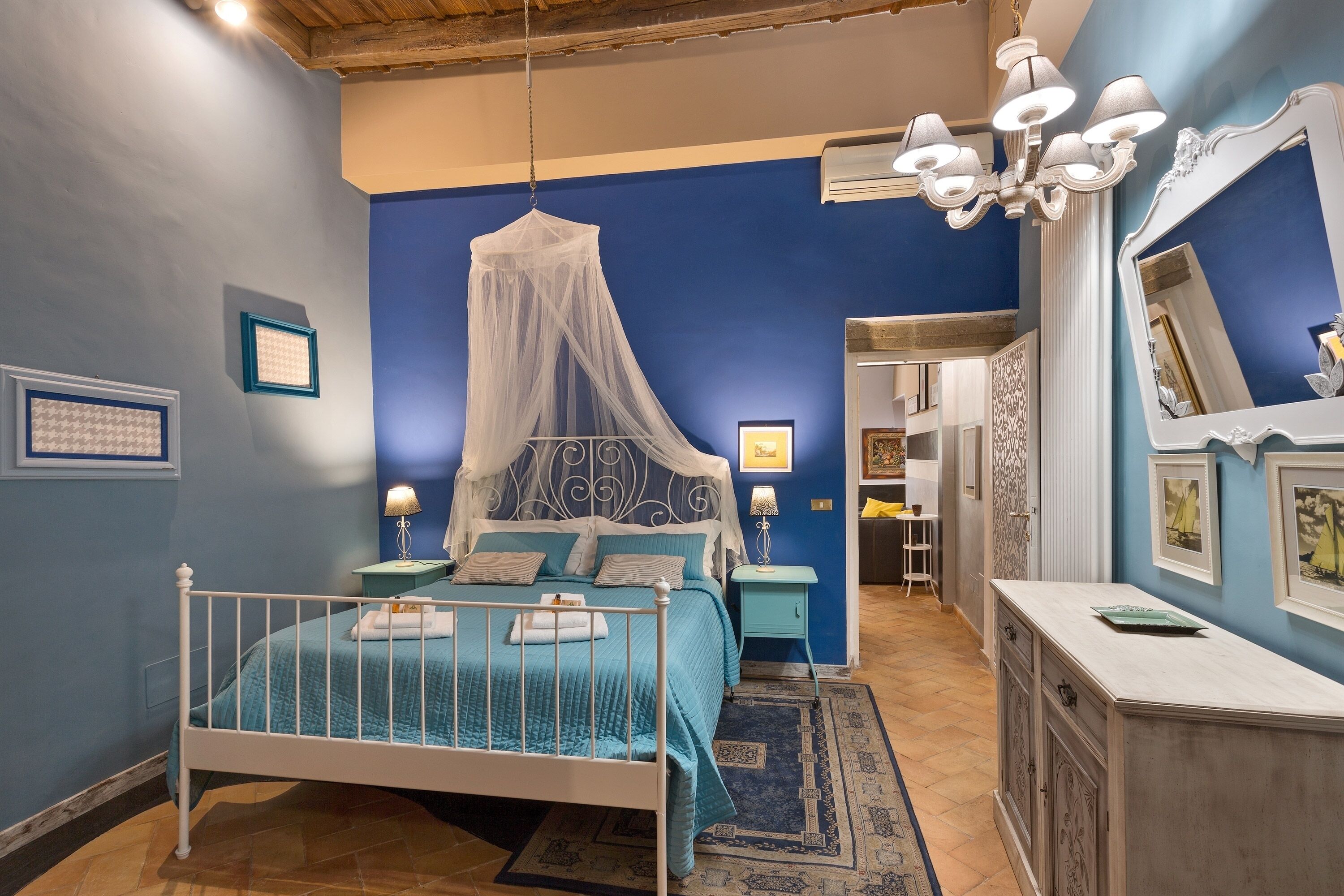 Un dormitorio con cama, mesita de noche, cómoda, espejo y candelabro.