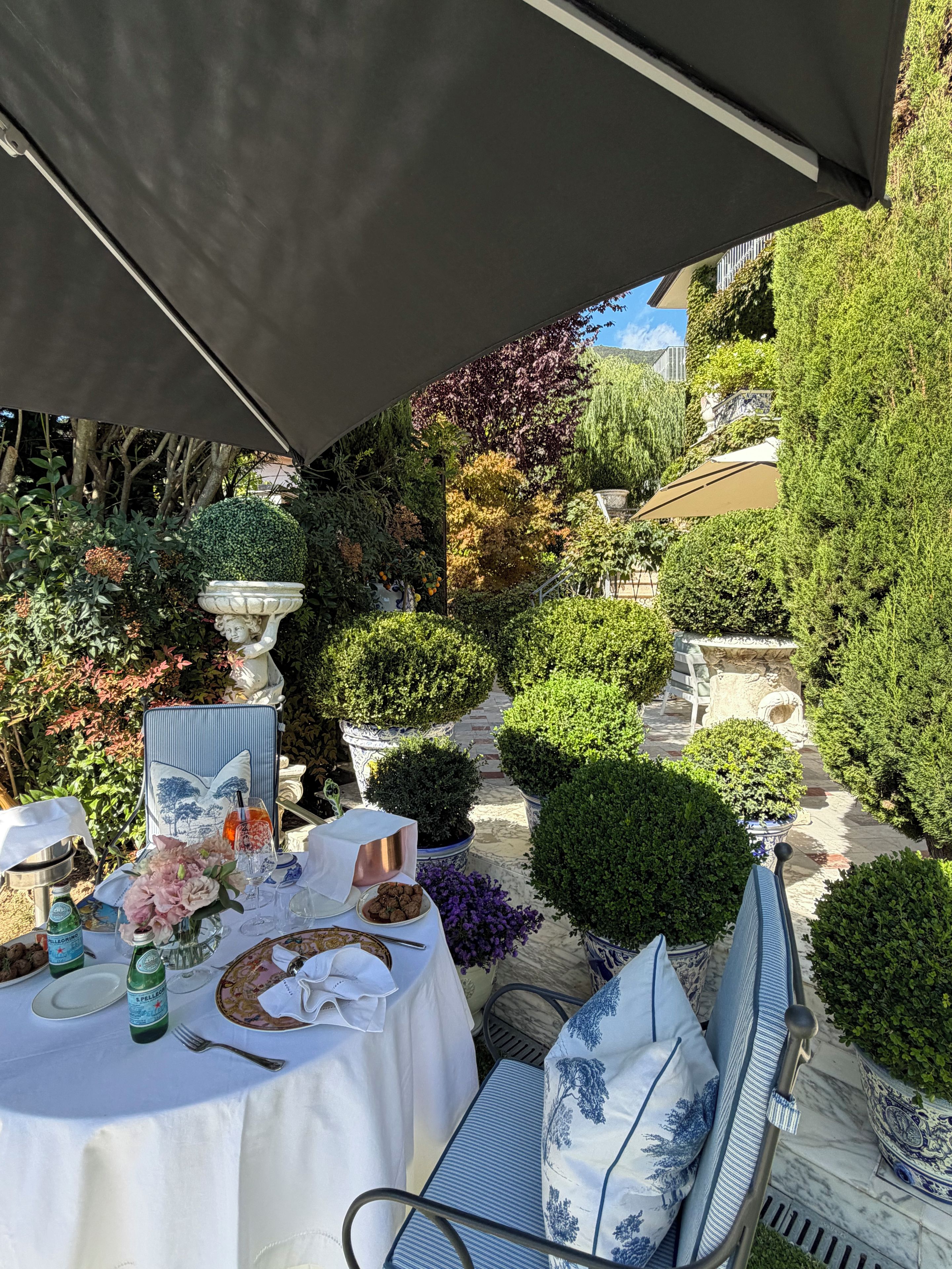 Een terras met eethoek, gedekt voor twee personen, omgeven door potplanten en een pad van stenen.