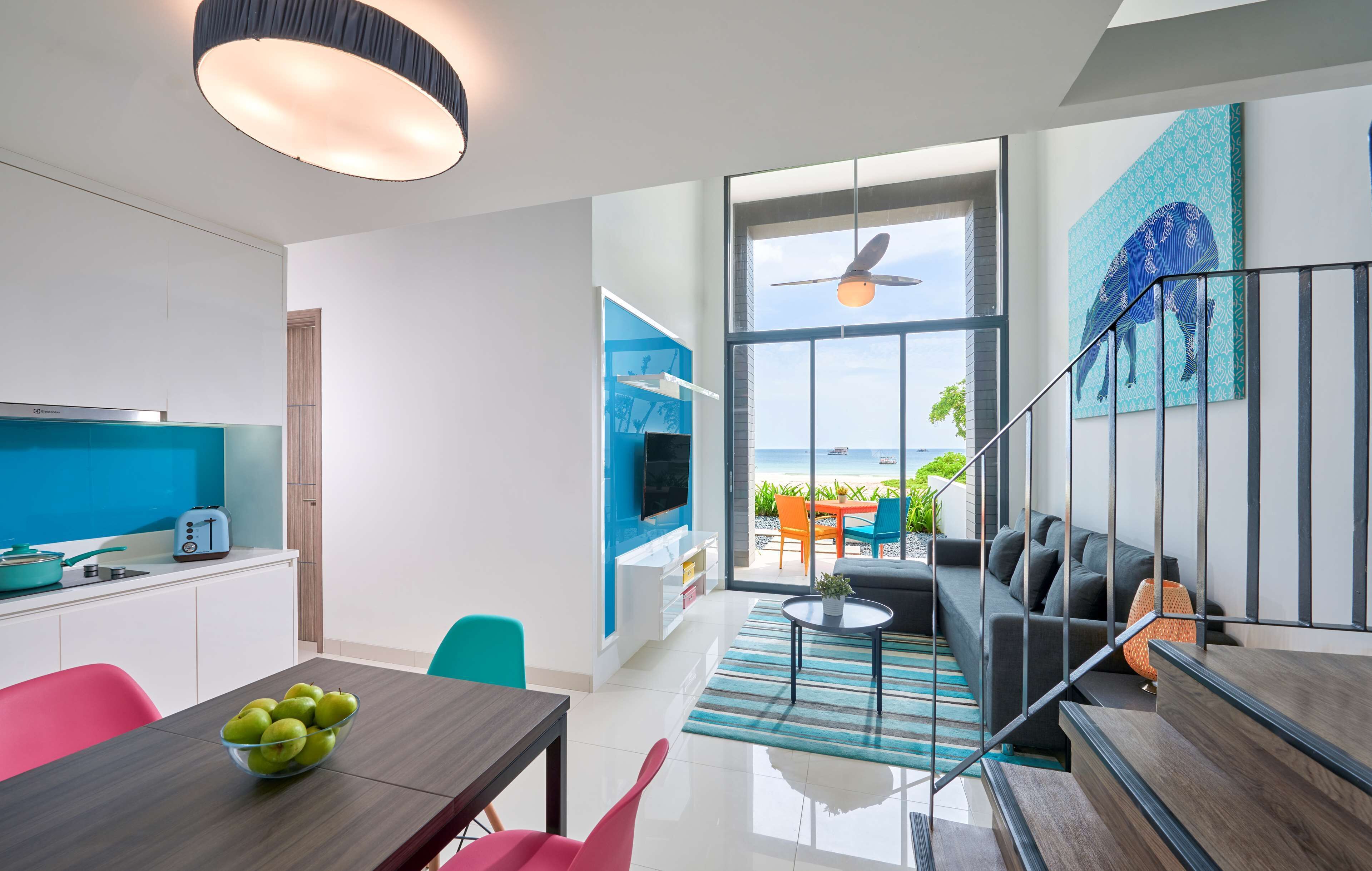A modern living room with a large window, a flat-screen TV, and a dining area with a table and chairs.