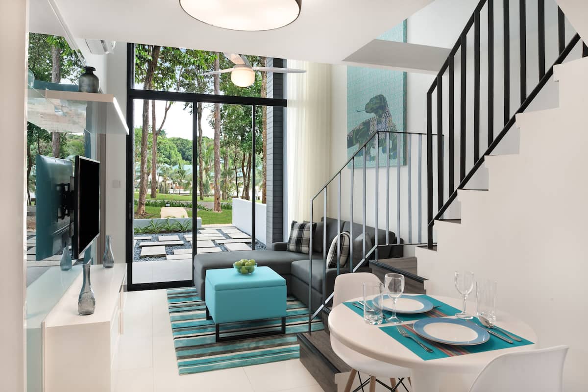 A modern living room with a sofa, ottoman, and dining table set for two.